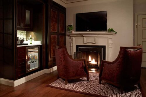 penthouse suite fireplace lit with two chairs bar area and cabinets