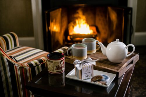 Hot chocolate and chocolates in a mug with a teapot on a table in front of a fire in a fireplace