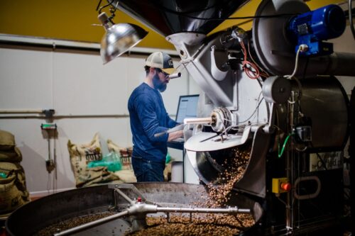 Man behind a coffee roasting machine with roasted coffee spilling out